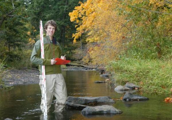 Smiling young man standing near a forest and stream